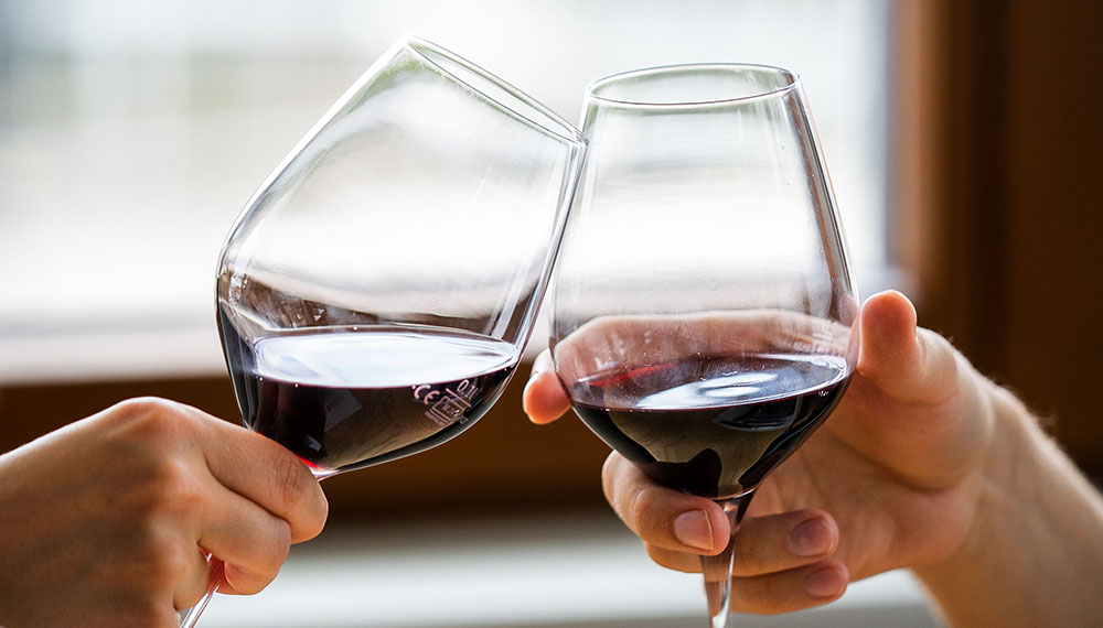 two people cheersing glasses of red wine