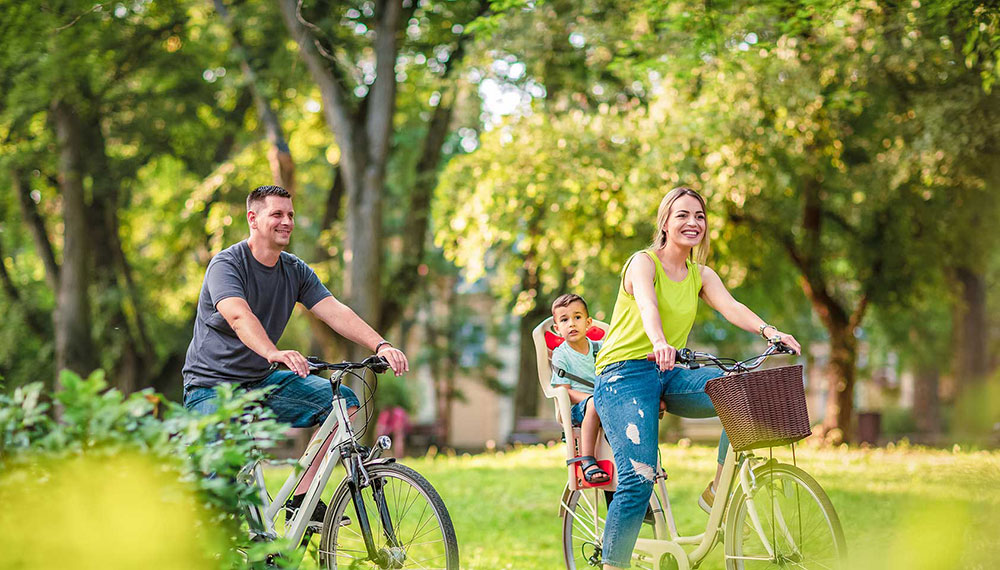 Couple riding bikes through the park with their son in a child seat
